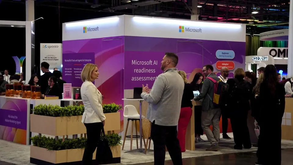A Microsoft stand on the show floor, its back wall reading 'Microsoft AI readiness assessment', attendees along a planted counter.