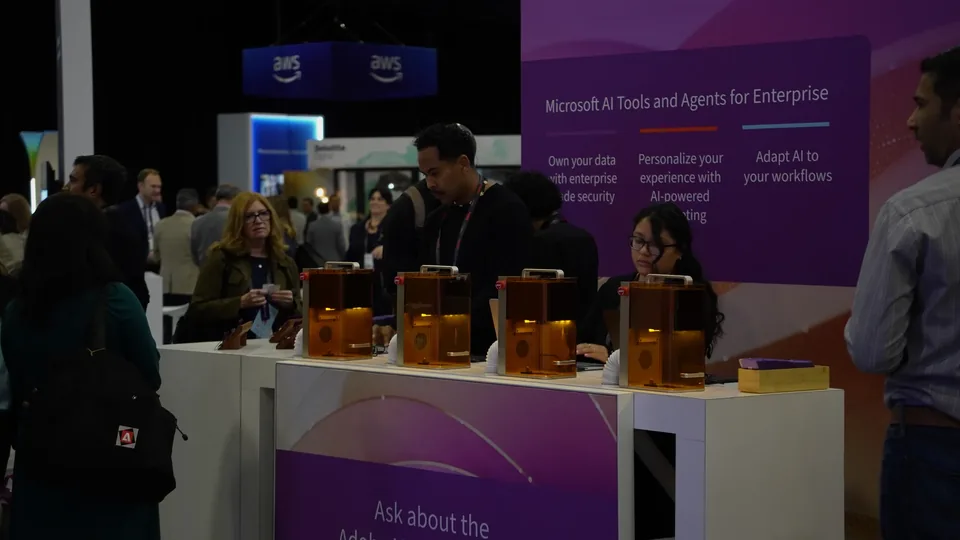 Attendees at a counter of amber-lit demo units, the wall behind reading 'Microsoft AI Tools and Agents for Enterprise'.