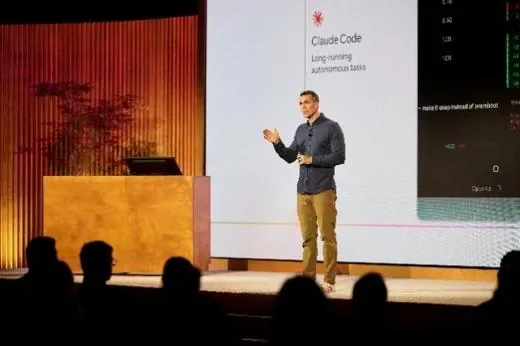 A speaker on stage presenting a slide on long-running autonomous coding tasks, the audience in silhouette.