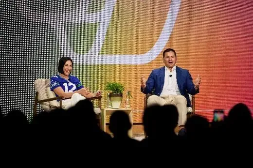 Two people in a stage conversation in front of a large LED wall.