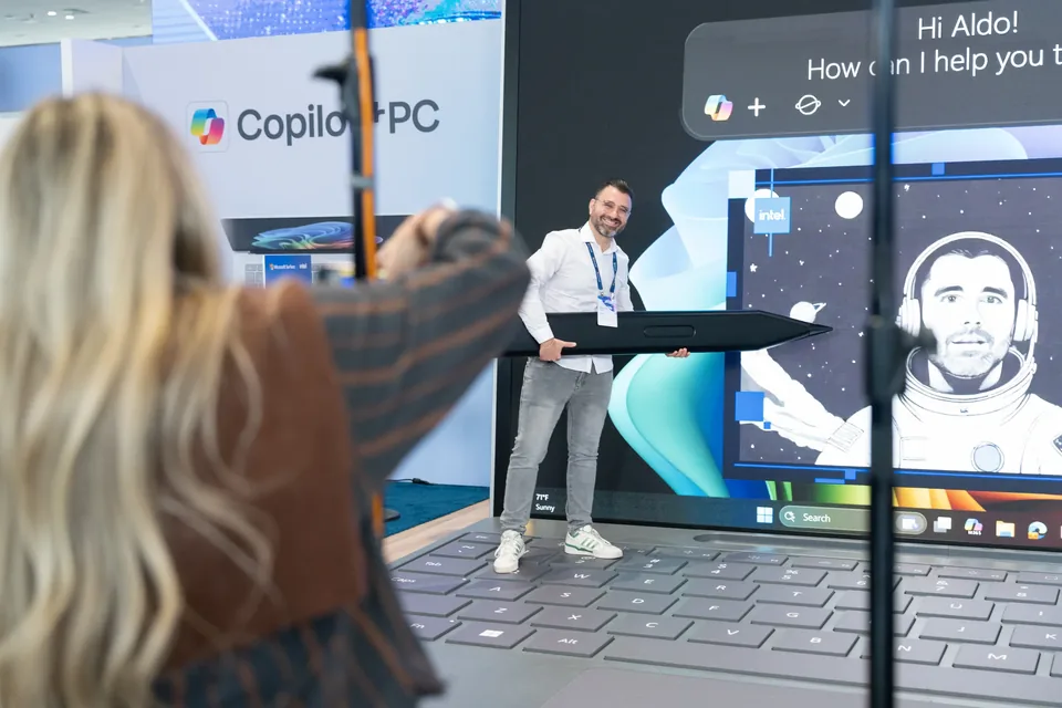 An attendee photographing a colleague posing with the oversized pen at the Copilot+ PC set.