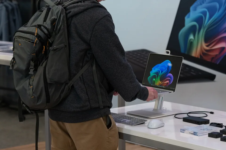A visitor with a backpack trying a Surface laptop at a white demo table.