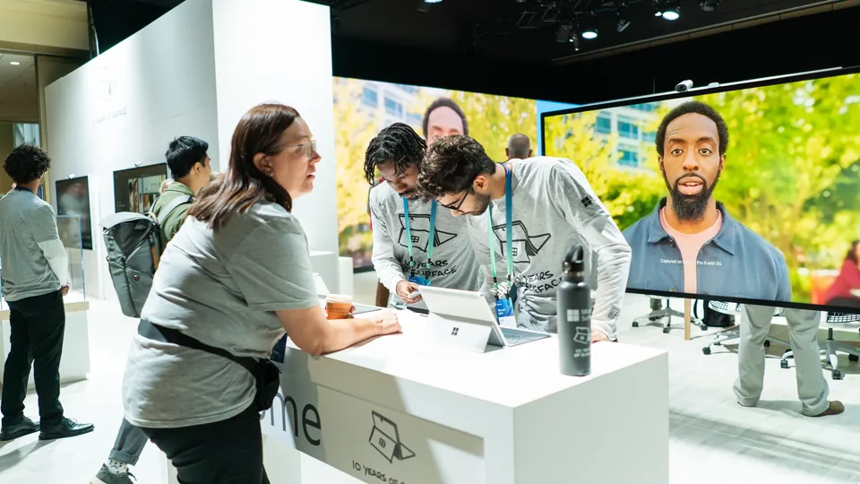 Attendees around a demo table in front of a wall-sized screen, staff in matching event shirts.