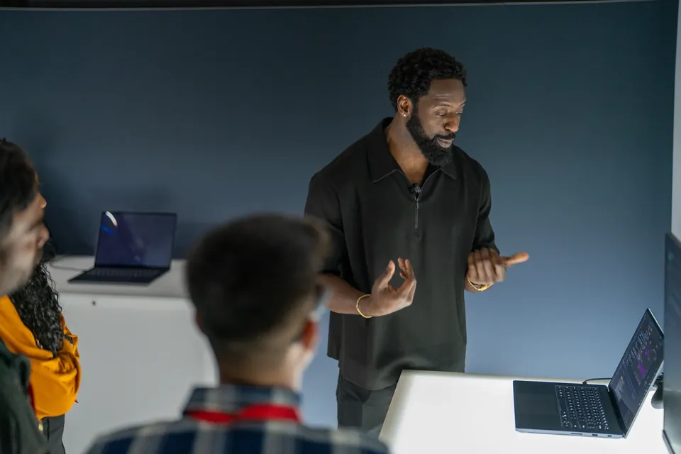 A speaker mid-sentence at a hands-on session, guests watching from the front row.